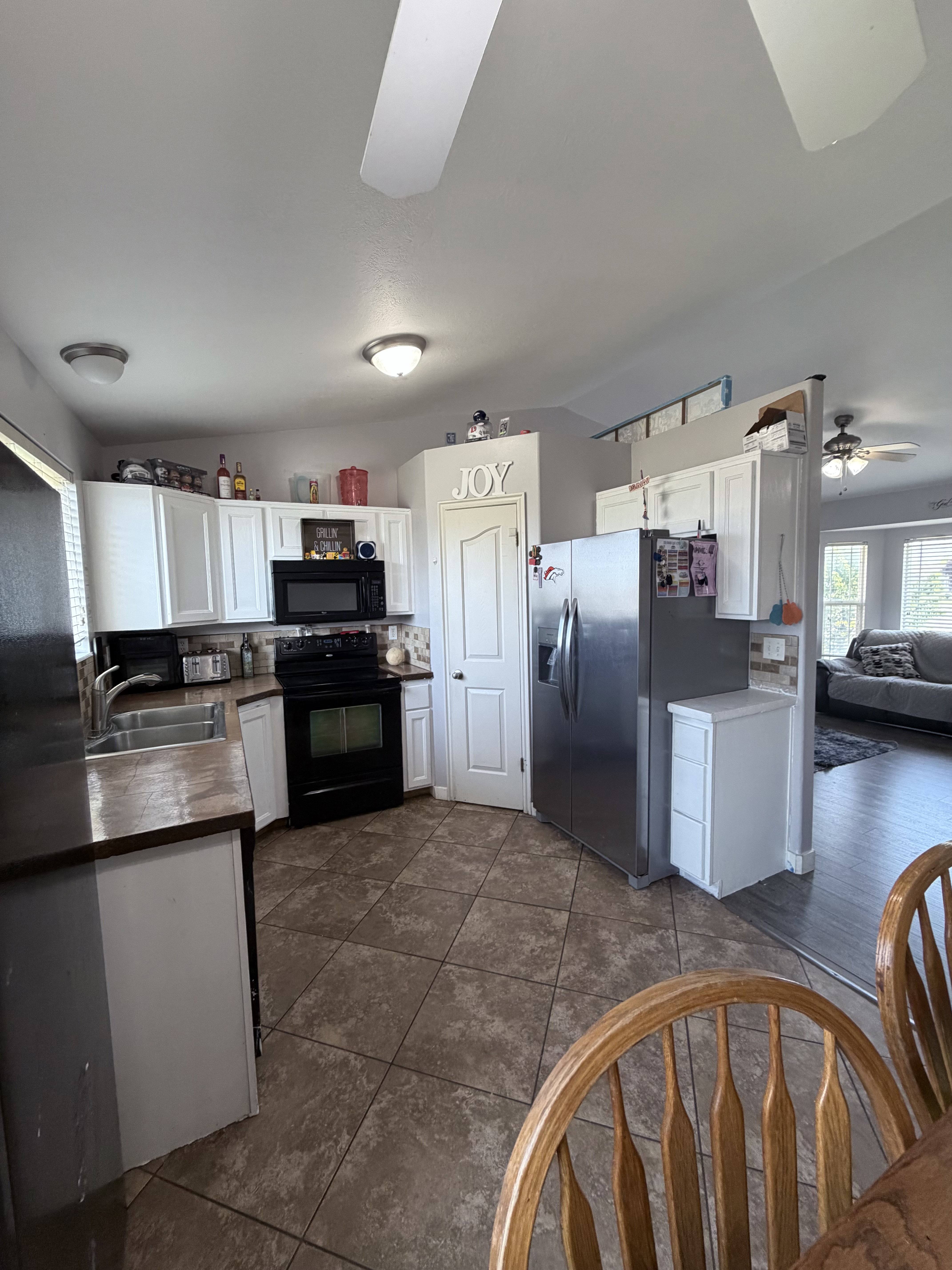 Kitchen featuring tile flooring, white cabinetry, dark countertops, black appliances, and a stainless steel refrigerator