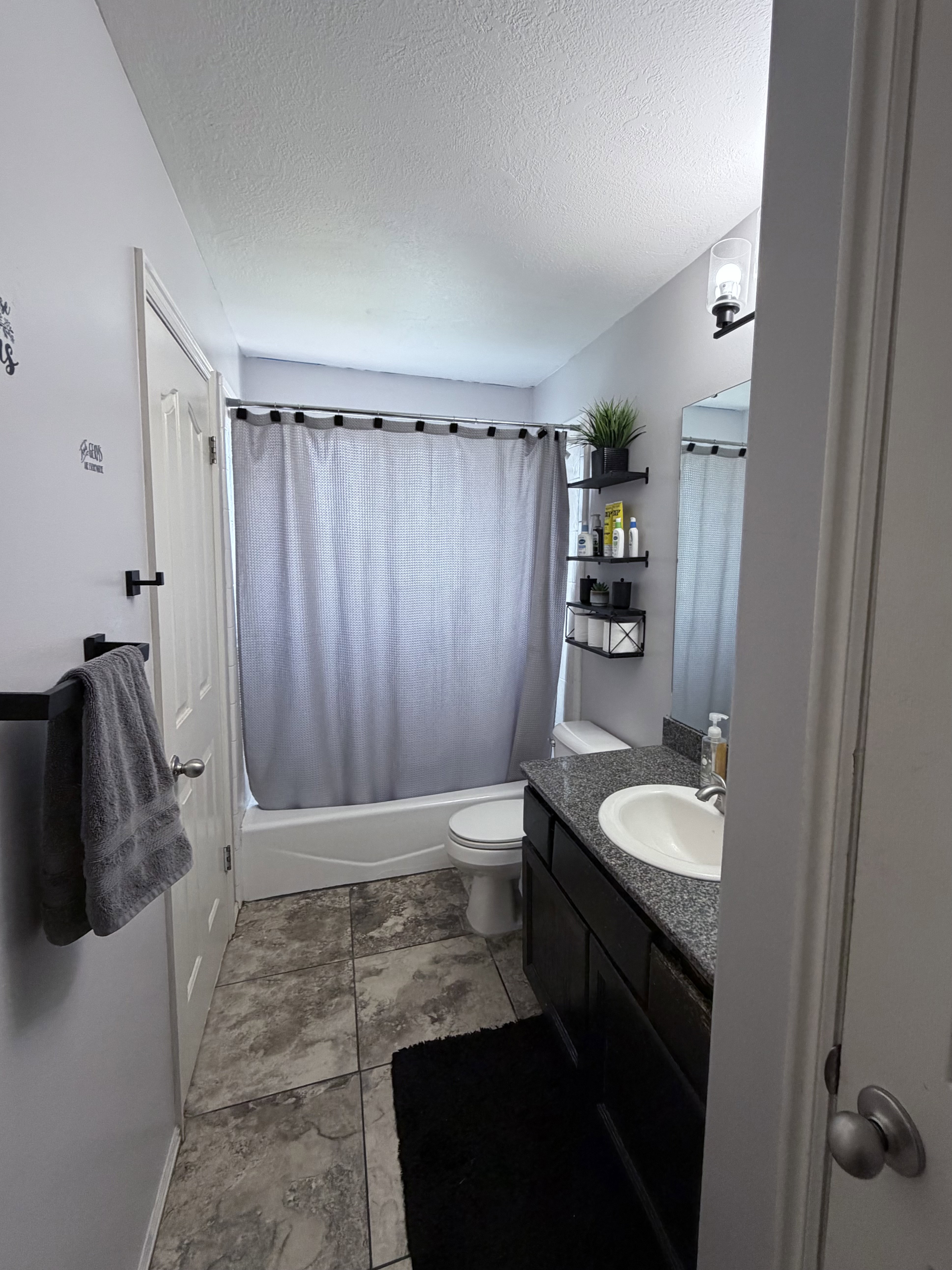 Bathroom featuring tile flooring, a white tub, a dark wood-finish vanity with a light-colored countertop, and a wall-mounted light fixture