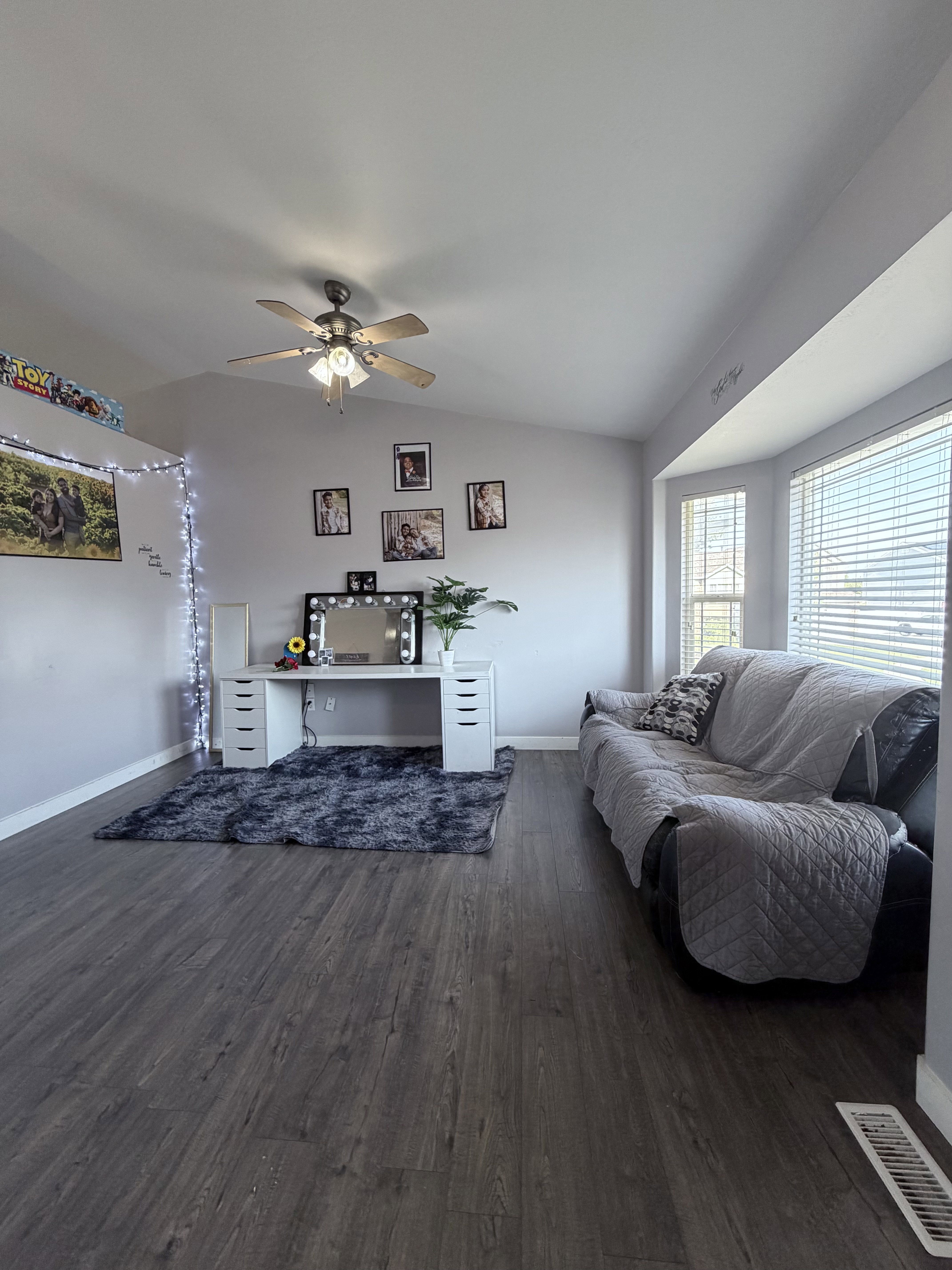 Vaulted ceilings enhance this room featuring dark wood-finish flooring, a ceiling fan, and large windows with blinds