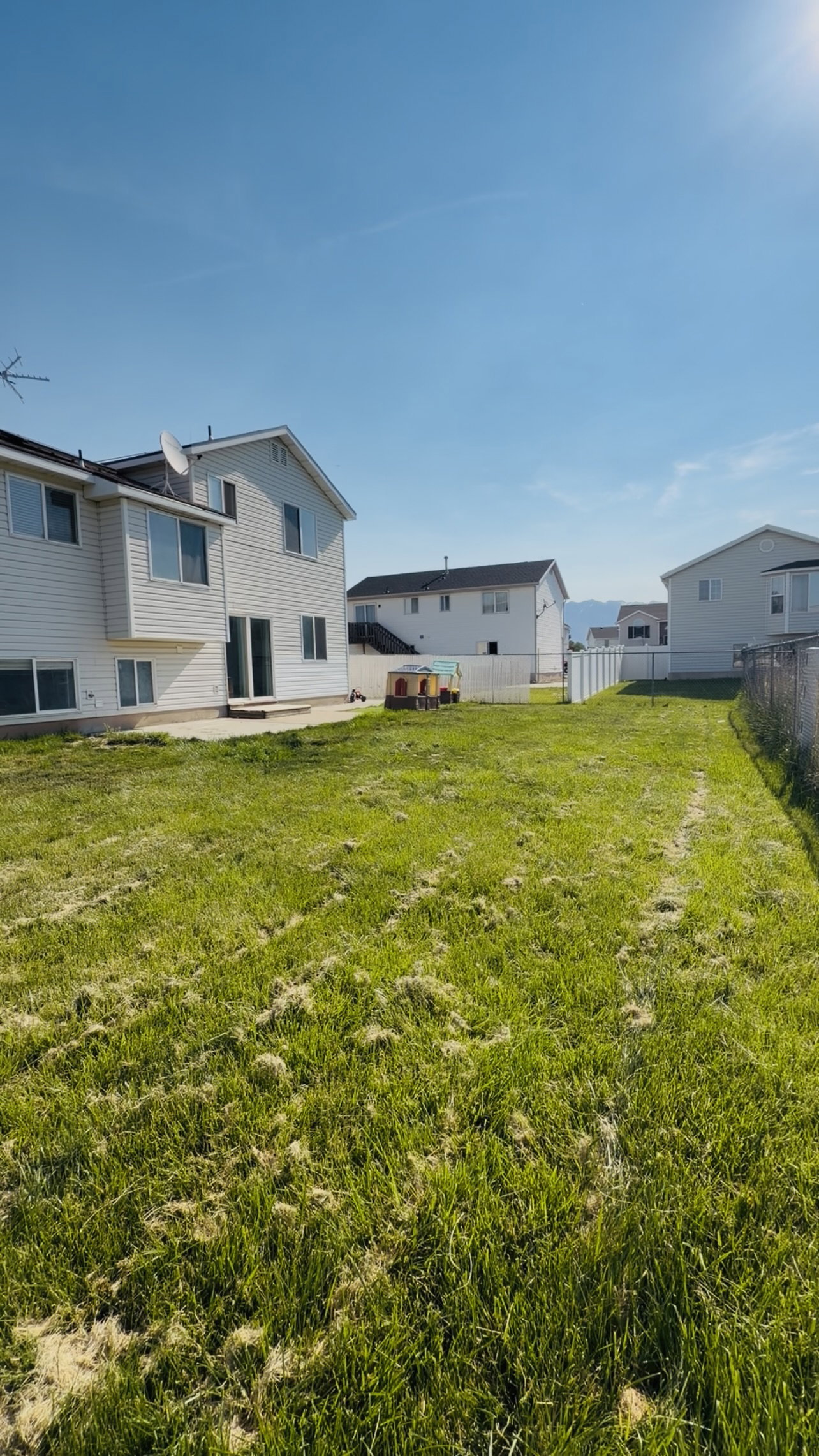 Spacious rear yard with a concrete patio, white vinyl fencing, and a chain-link fence