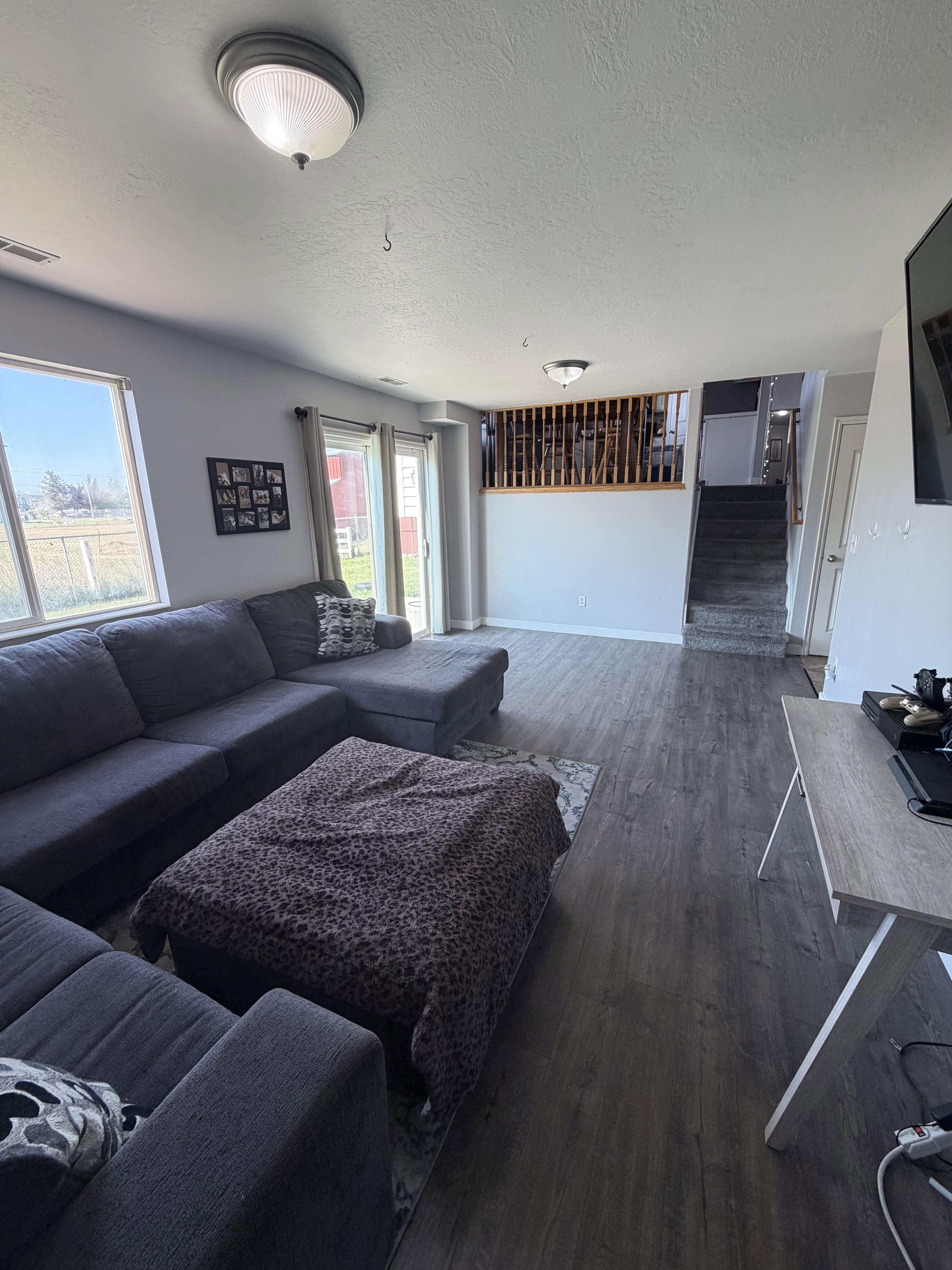 Spacious living area featuring wood-finish flooring, light gray wall tones, and multiple windows