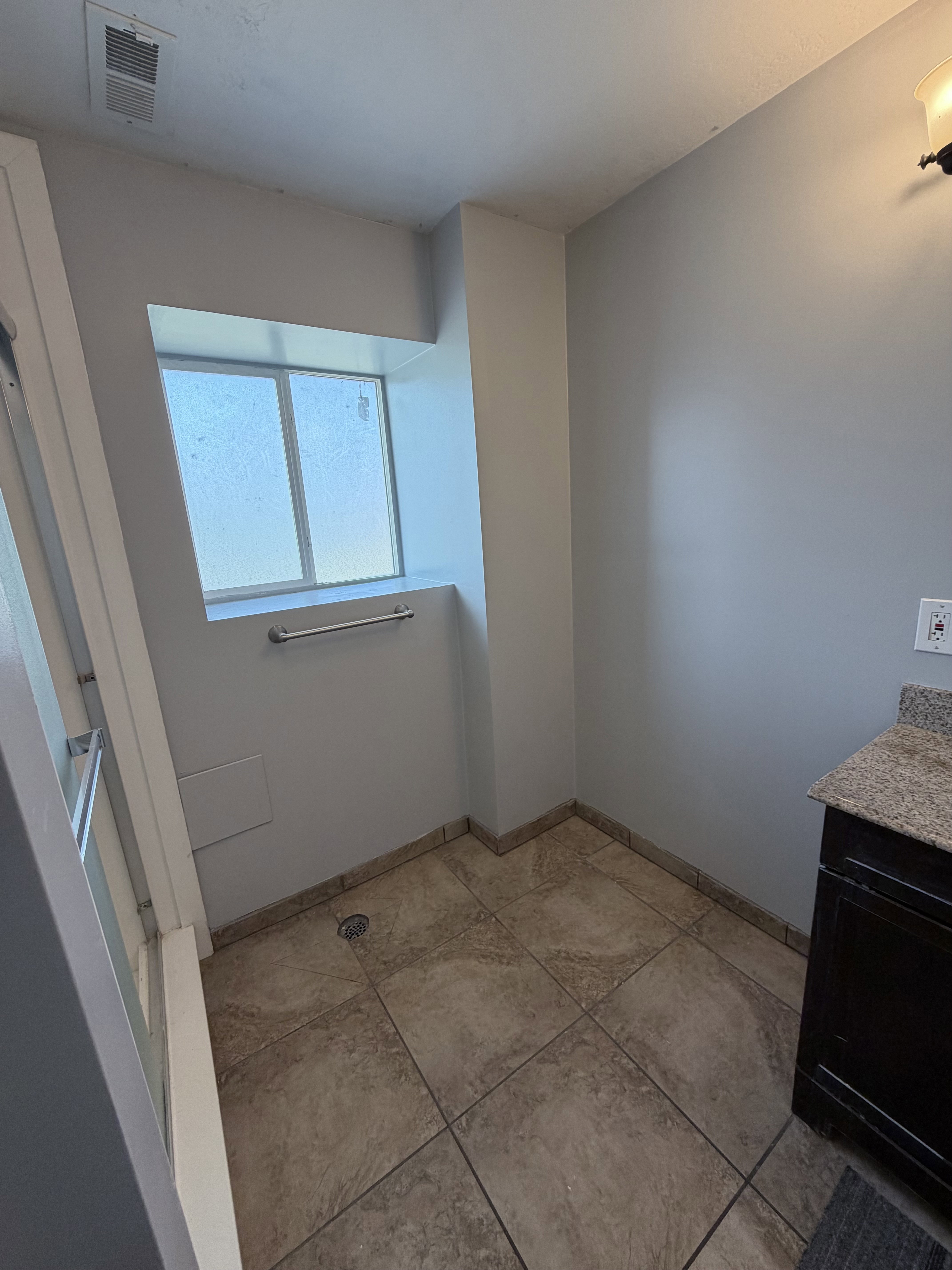 Bathroom featuring a tiled shower area, a window, and a dark wood-finish vanity with a granite-style countertop