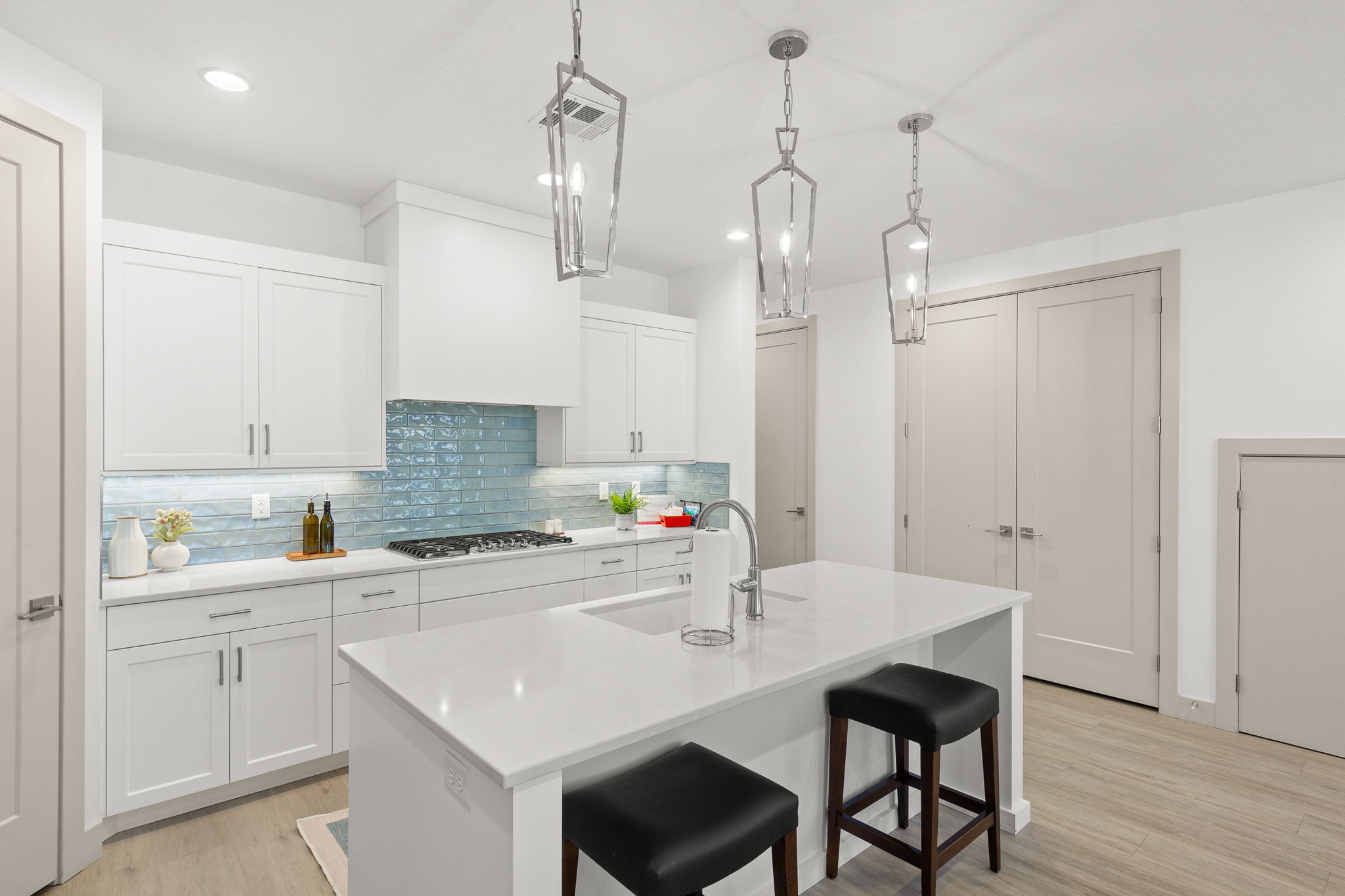 Contemporary kitchen featuring white shaker cabinetry, an expansive center island with seating, a gas range, a unique blue glass tile backsplash, and three geometric pendant lights