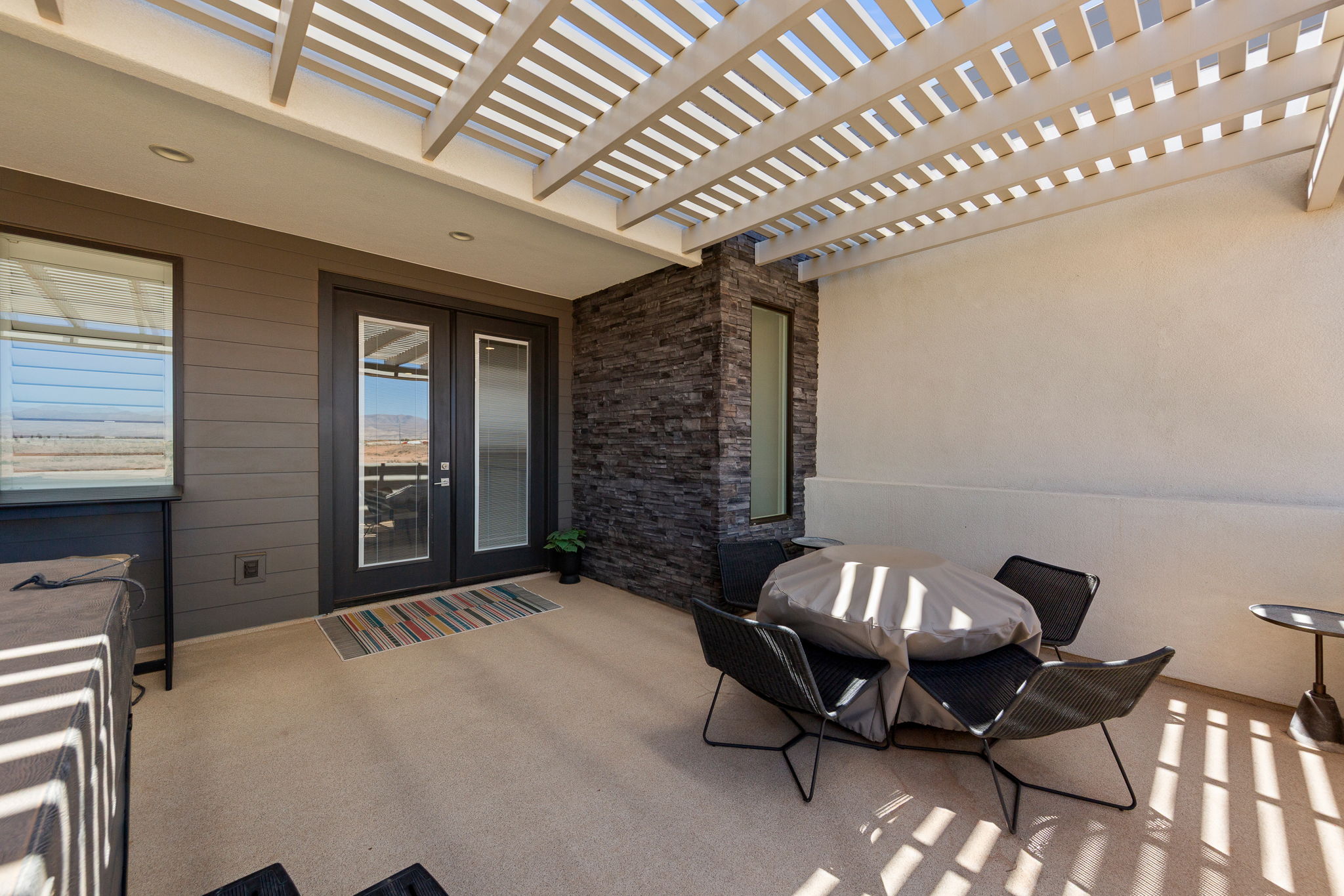 Outdoor patio featuring a slatted pergola, textured stone accent wall, and double glass-panel doors