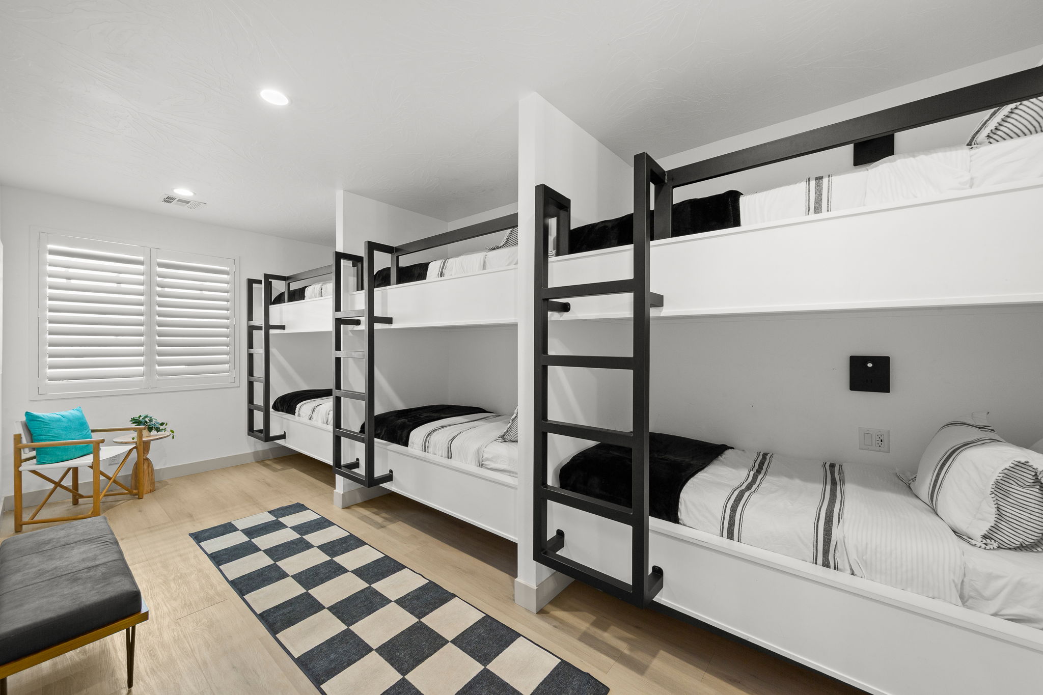 Built-in bunk beds with black metal ladders, recessed ceiling lighting, plantation shutters, and wood-finish flooring