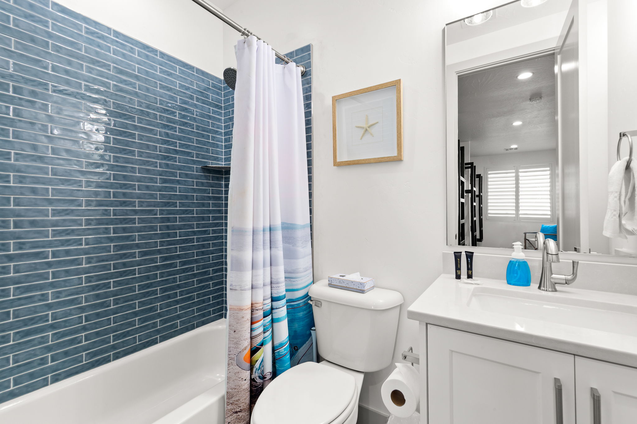 Full bathroom featuring a tub-shower combination with blue subway tile surround, white vanity with integrated sink, and wall-mounted mirror