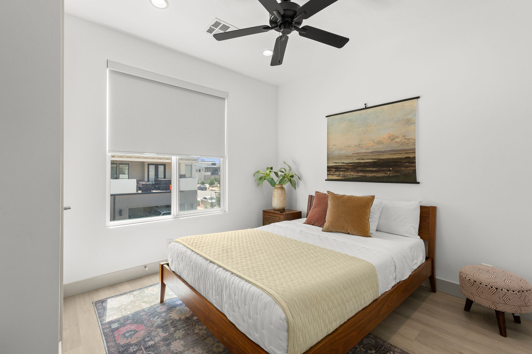 Bright bedroom featuring light wood-finish flooring, a contemporary ceiling fan, recessed lighting, and a window with a roller shade
