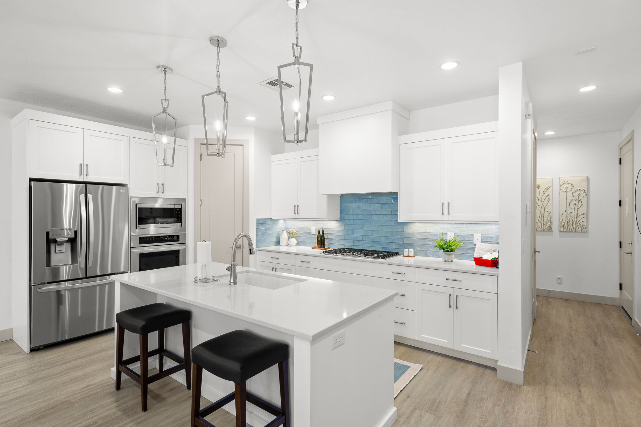 Kitchen featuring an expansive island with an undermount sink, white cabinetry, a blue tile backsplash, stainless steel appliances, and wood-finish flooring