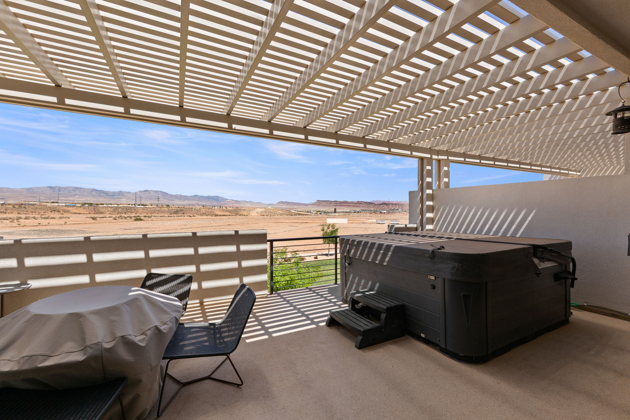 Expansive outdoor patio featuring a slatted pergola, a built-in hot tub, and concrete flooring