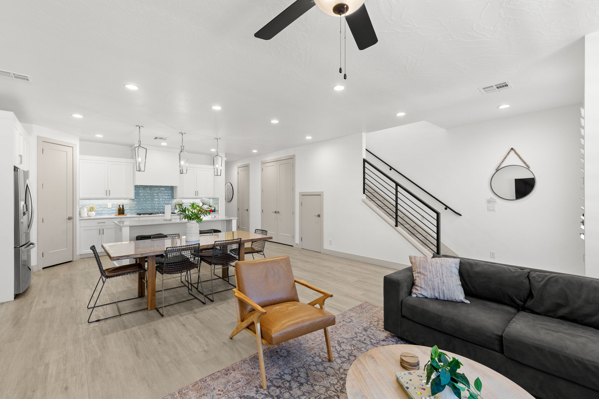 Open-concept living space featuring light wood-finish flooring, recessed lighting, and a modern kitchen with a blue subway tile backsplash