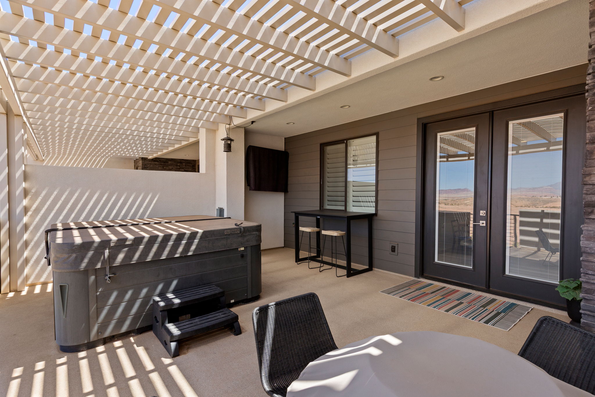 Spacious patio featuring a louvered pergola, built-in hot tub, and stone accent column