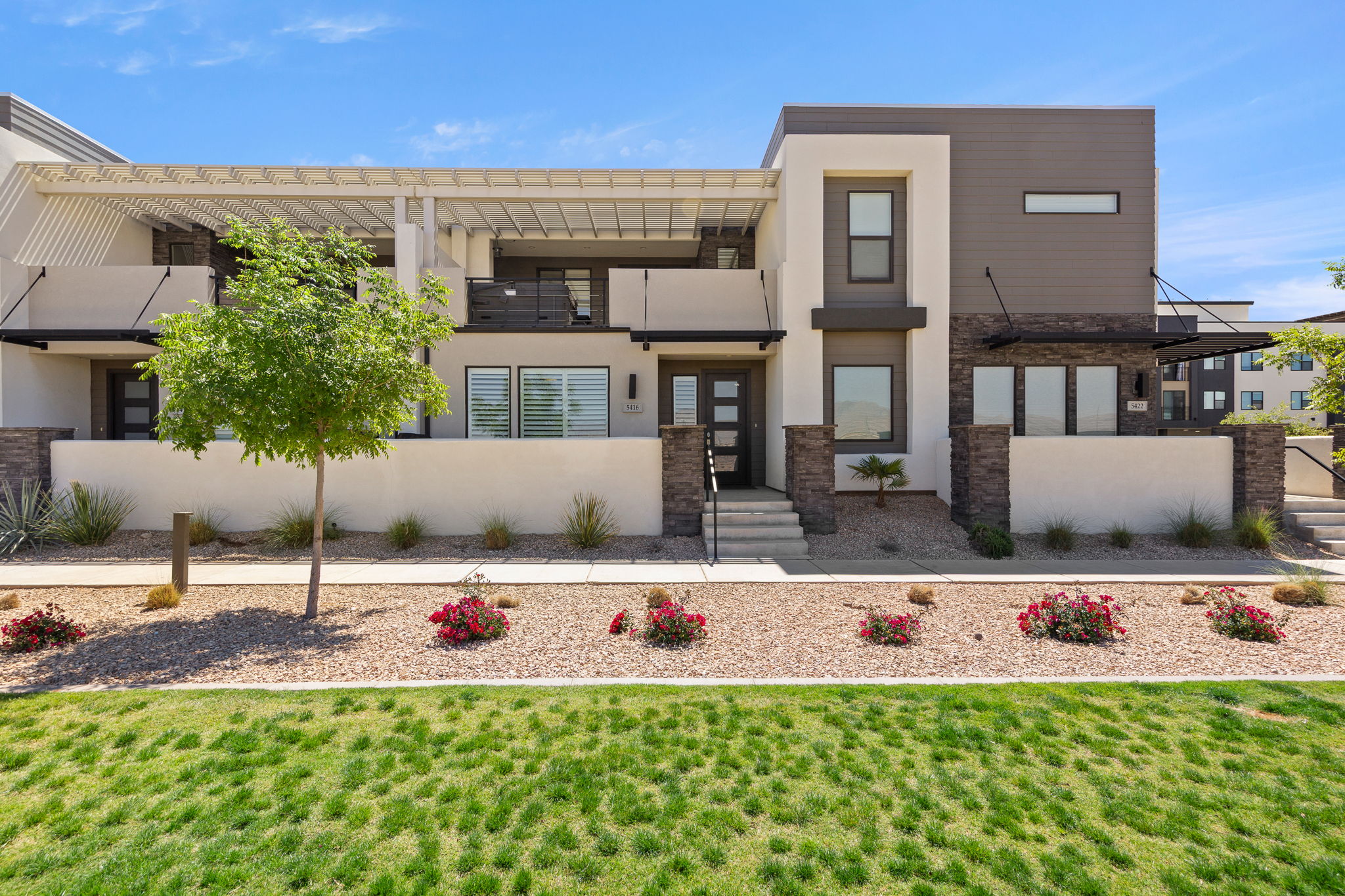 Contemporary multi-story facade featuring varied paneling, stone accents, and a slatted pergola