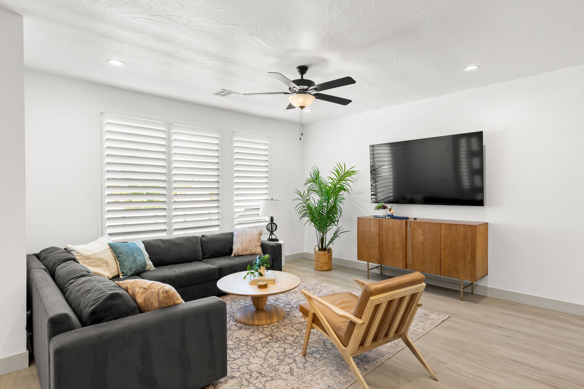 Bright living space featuring multiple windows with plantation shutters, recessed lighting, and a ceiling fan with integrated lighting