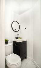 Compact powder room featuring a black vanity with a white countertop, a round black-framed mirror, a black wall-mounted faucet, and a white toilet