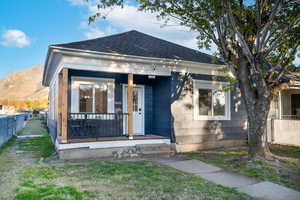 Charming bungalow featuring a covered front porch with dark railing, a prominent front door, and a shingle roof