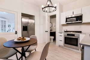 Kitchen featuring white cabinetry, stainless steel appliances, light wood-finish flooring, and a contemporary black chandelier