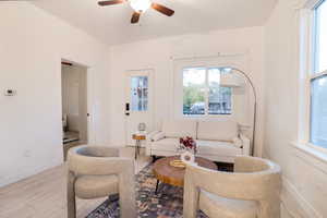 Bright living area featuring wood-finish flooring, a ceiling fan with integrated lighting, and multiple windows
