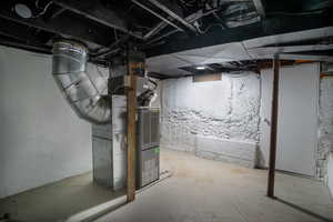 Utility room featuring a forced-air furnace, exposed ceiling joists, concrete flooring, and painted foundation walls