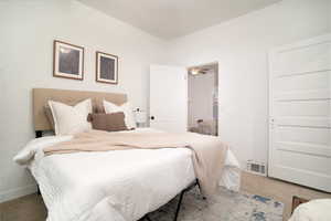 Carpeted bedroom featuring a textured rug, white walls, and a five-panel interior door
