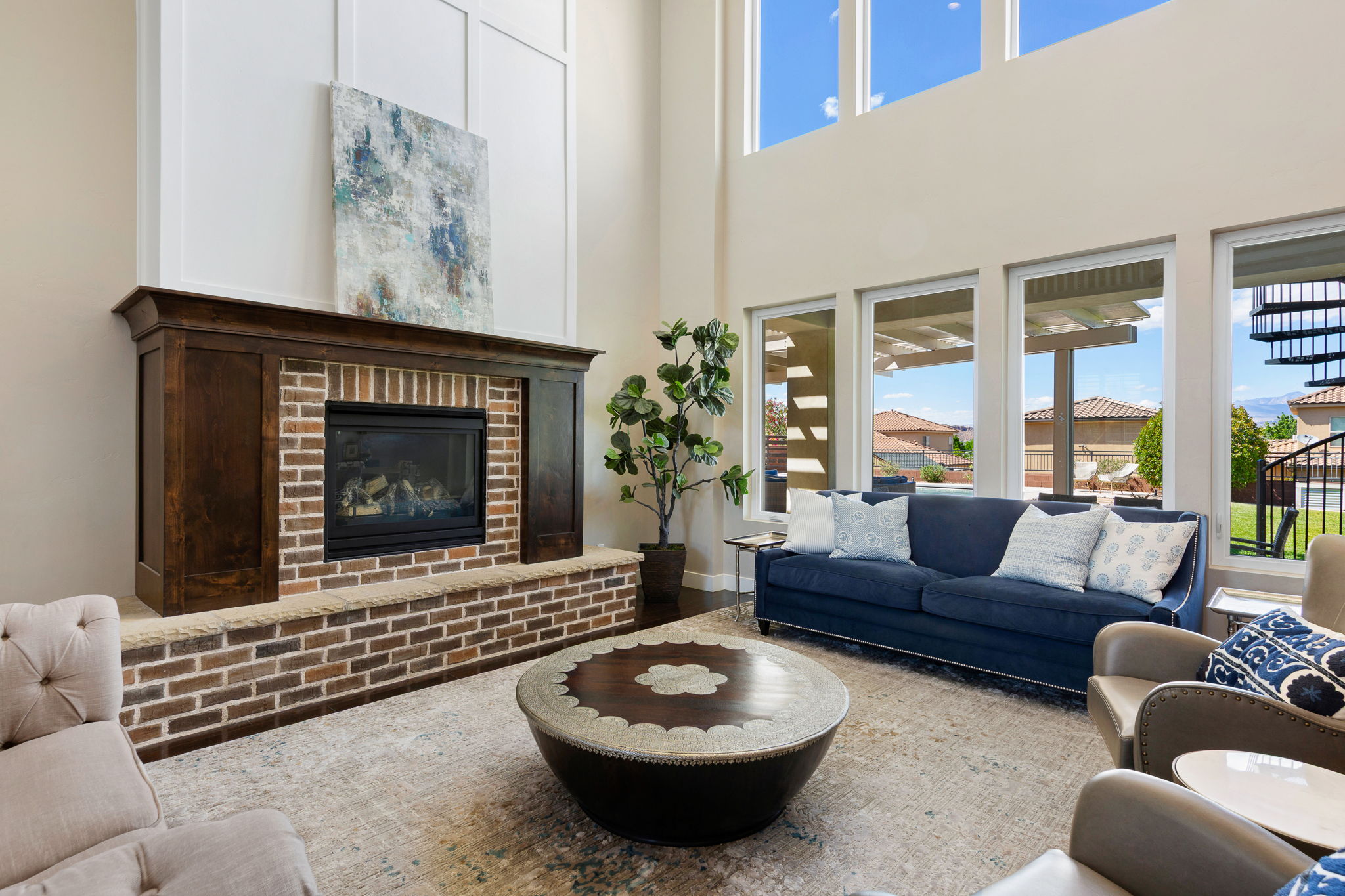Spacious living area featuring a prominent brick fireplace with a dark wood mantle, soaring ceilings, and expansive windows