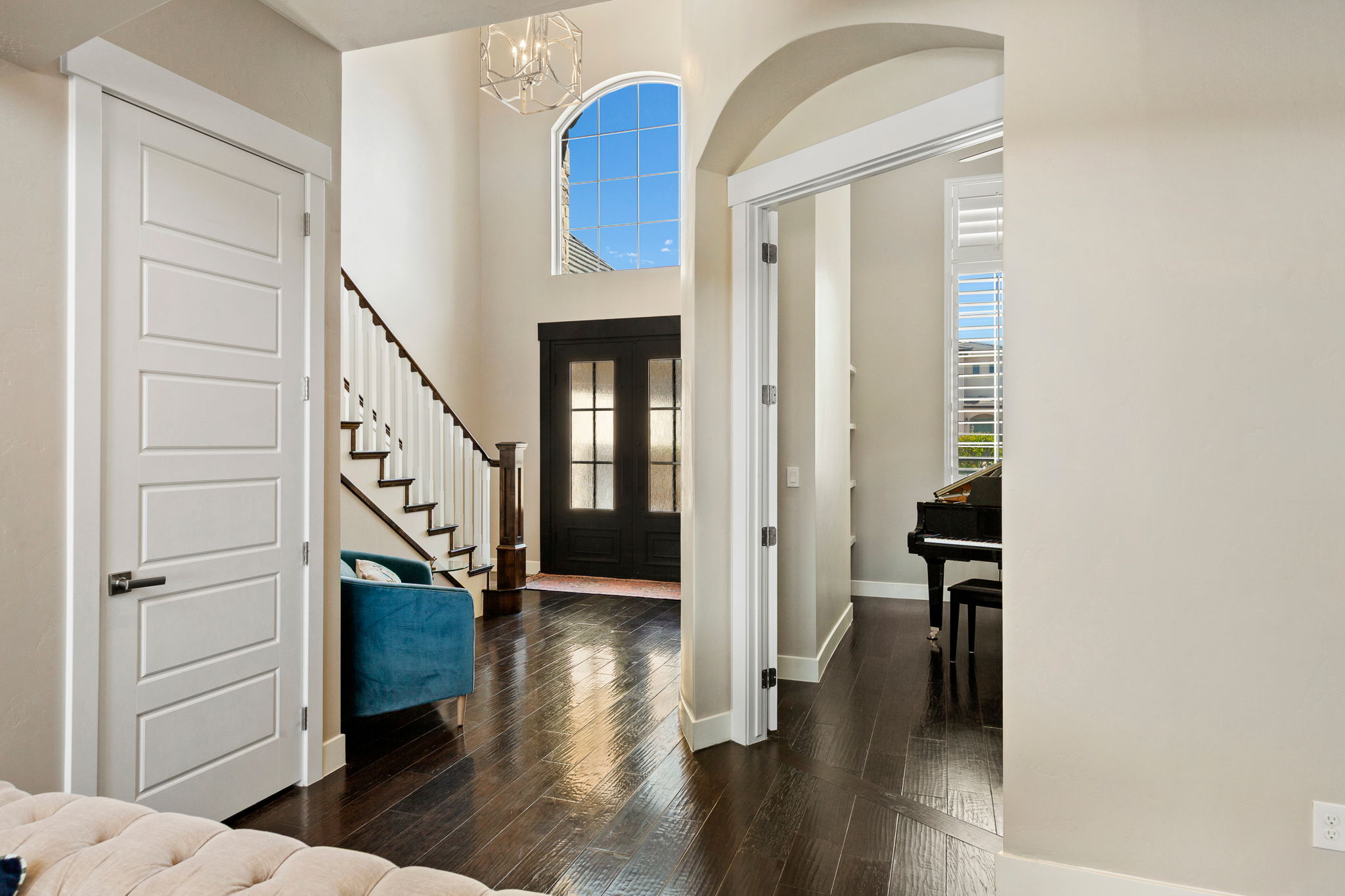 Grand entryway featuring dark wood-finish flooring, a contemporary chandelier, and a prominent arched window
