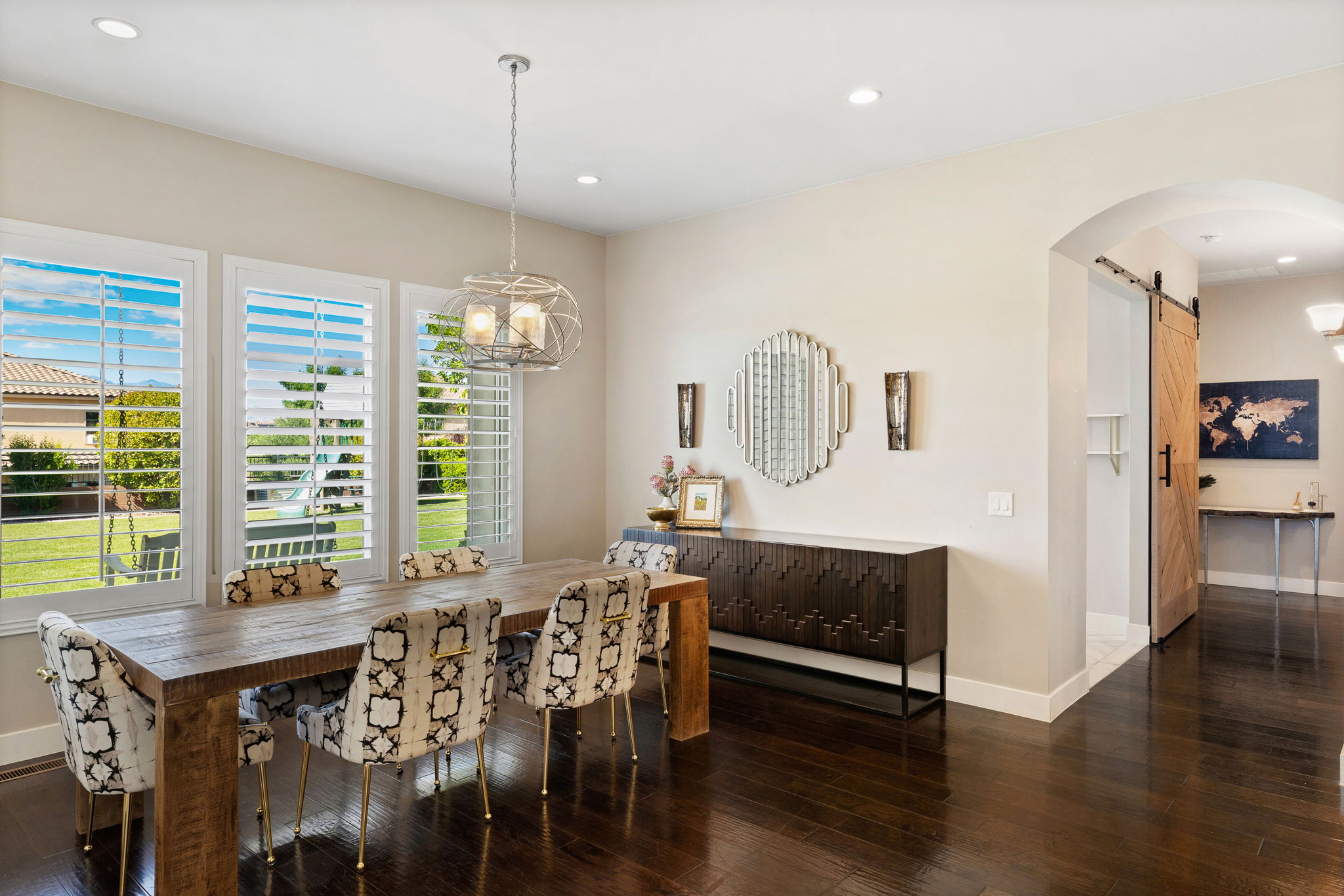 Dining area featuring dark wood-finish flooring, three large windows with white louvered shutters, and a modern geometric pendant light fixture