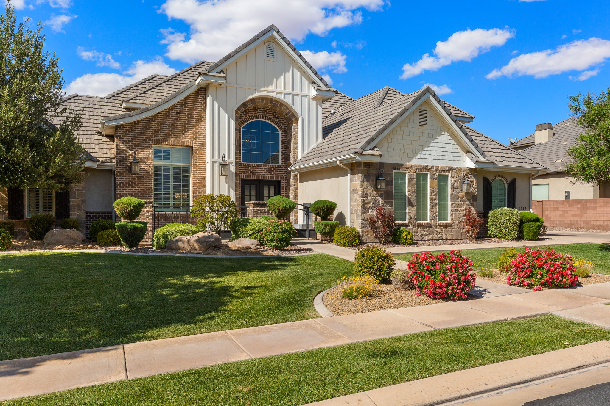 Exterior featuring brick and stone masonry, a multi-gabled roofline with dimensional shingles, an arched window above double entry doors, and board and batten siding accents