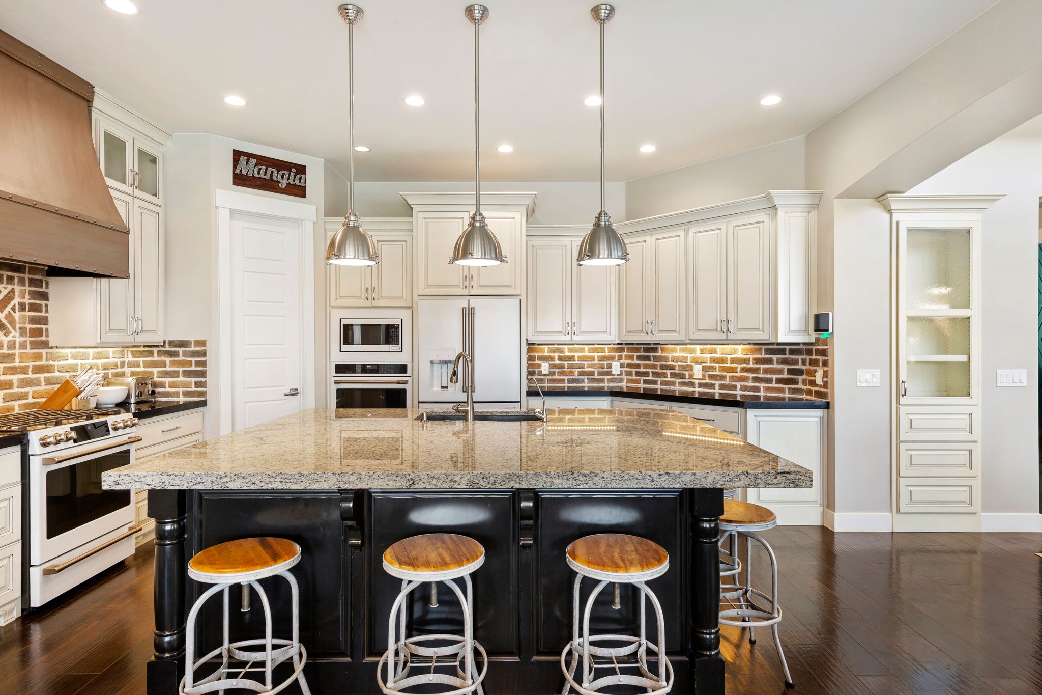 Spacious kitchen featuring a large island with a stone-finish countertop, white cabinetry, a brick-style backsplash, stainless steel appliances, and dark wood-finish flooring