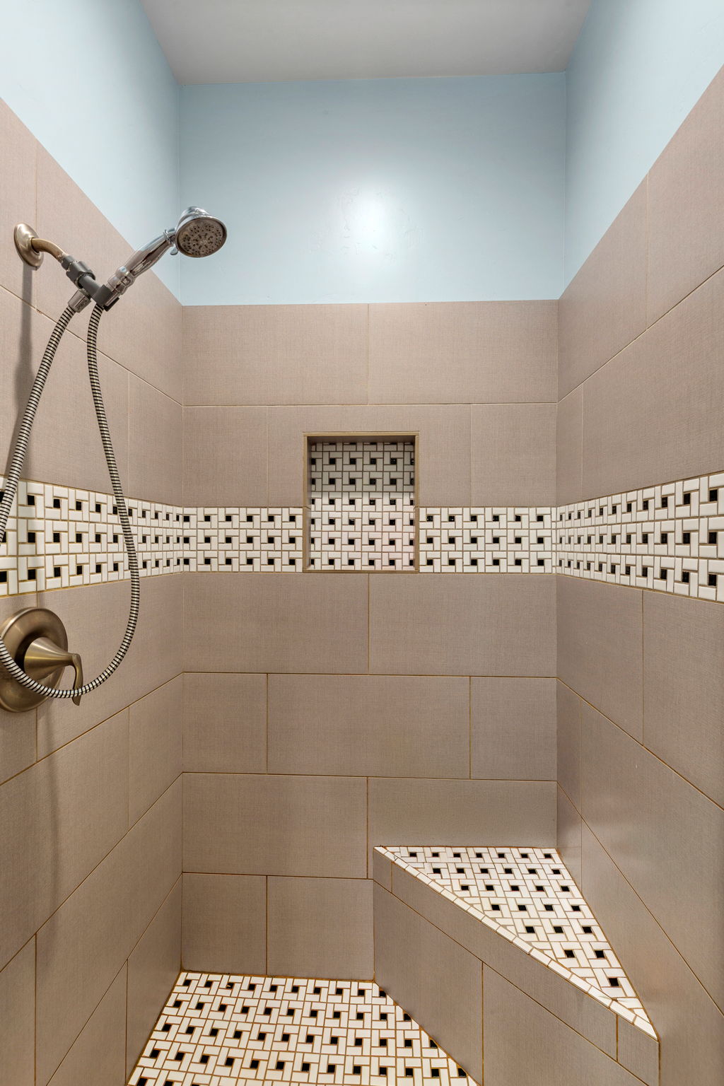 Shower stall with large format wall tiling, a decorative mosaic accent band, and a built-in bench
