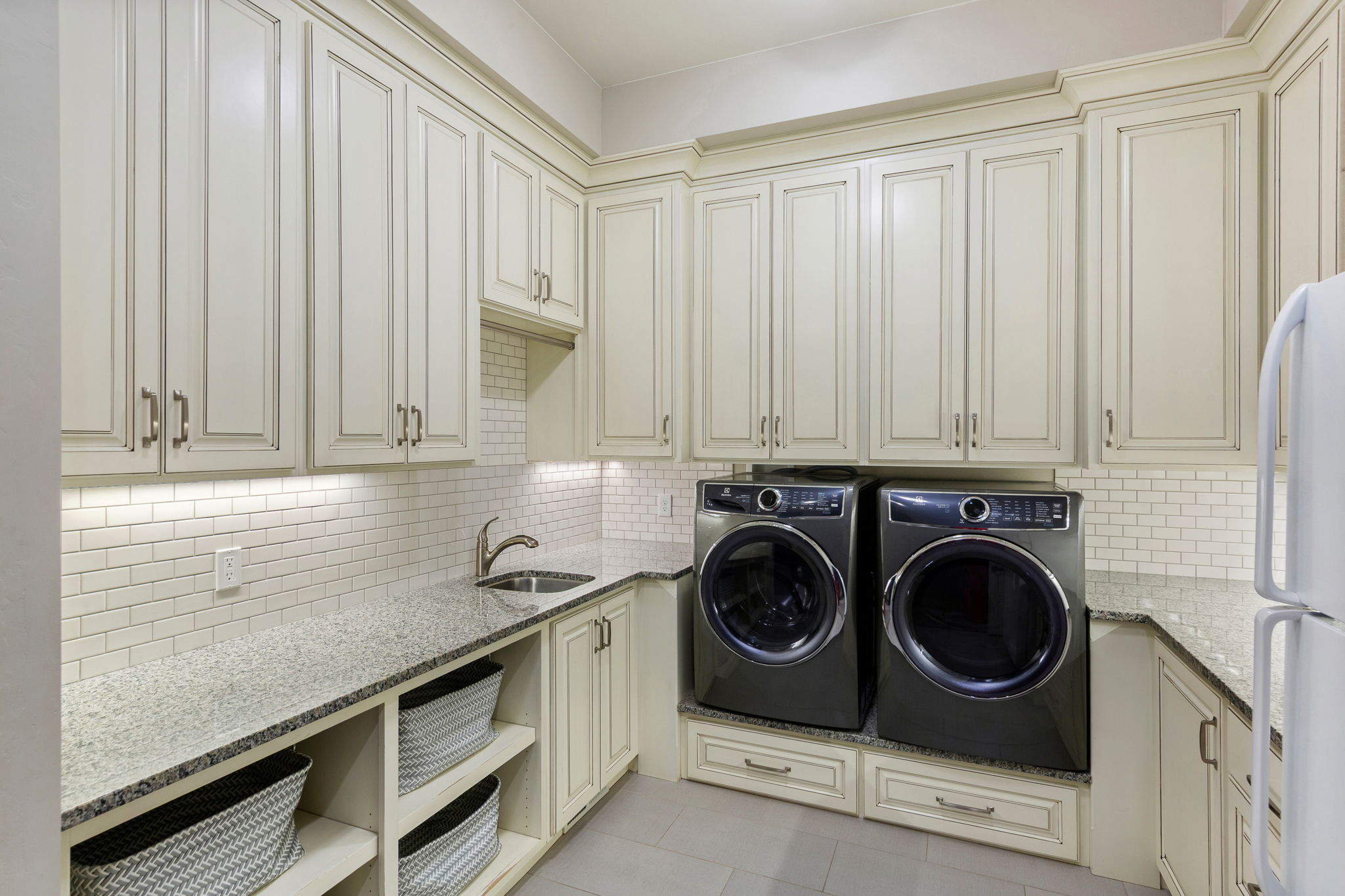 Laundry room featuring extensive custom cabinetry, light-toned granite countertops, a white subway tile backsplash, and an undermount sink