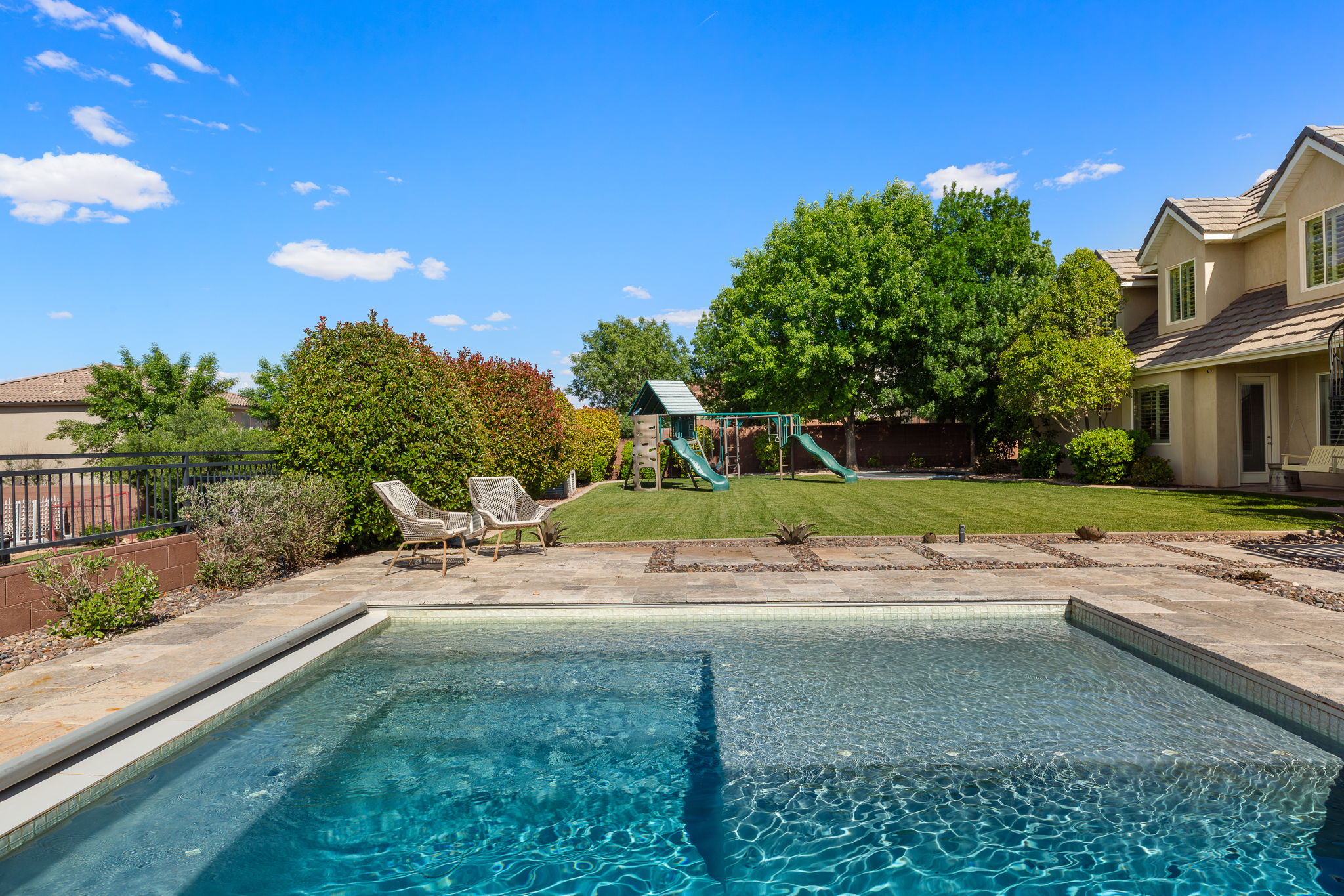 Backyard oasis featuring a swimming pool with integrated tanning ledge, stone paver patio, expansive lawn, and mature landscaping