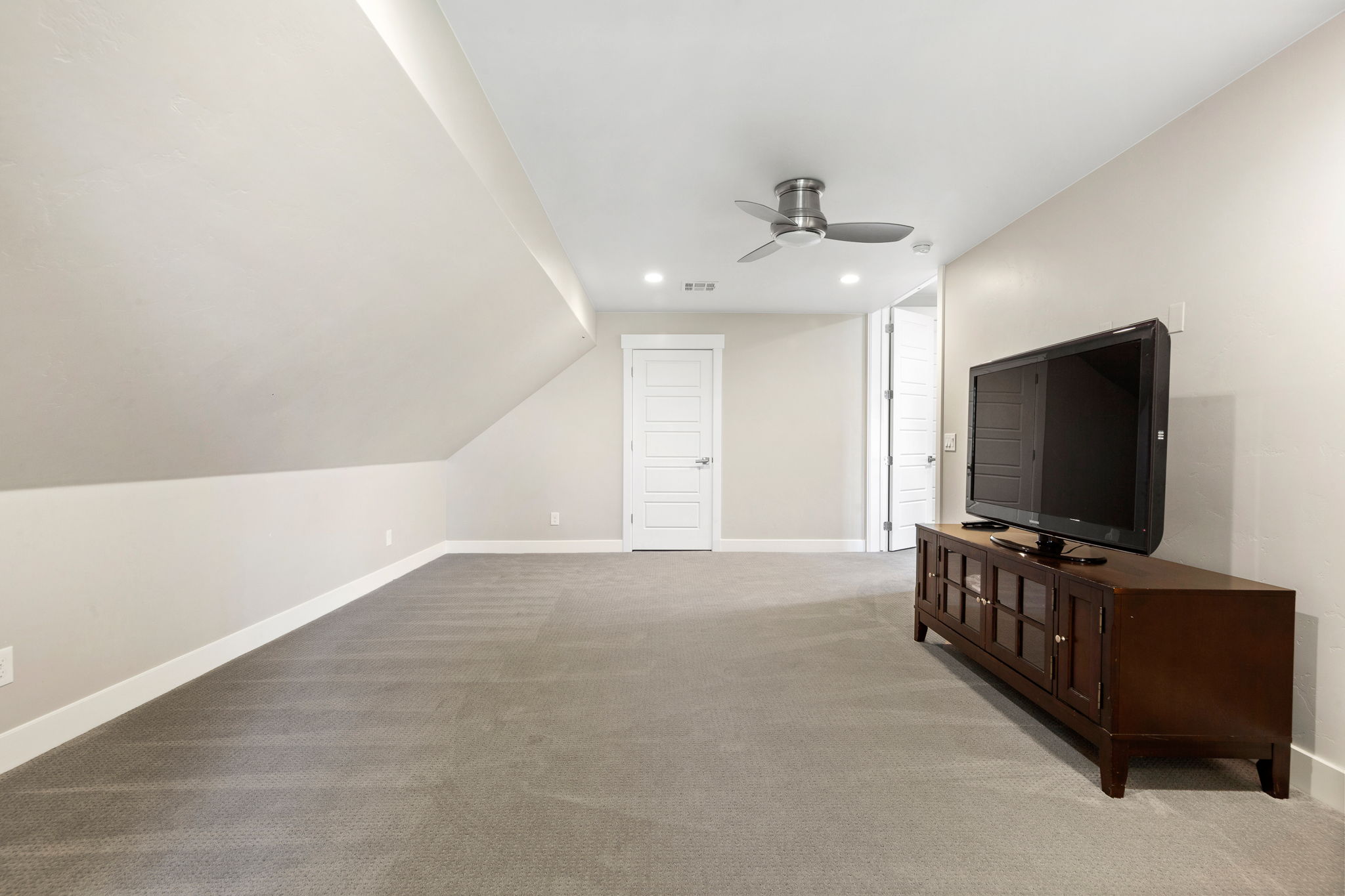 Spacious carpeted room featuring a sloped ceiling, recessed lighting, and a ceiling fan
