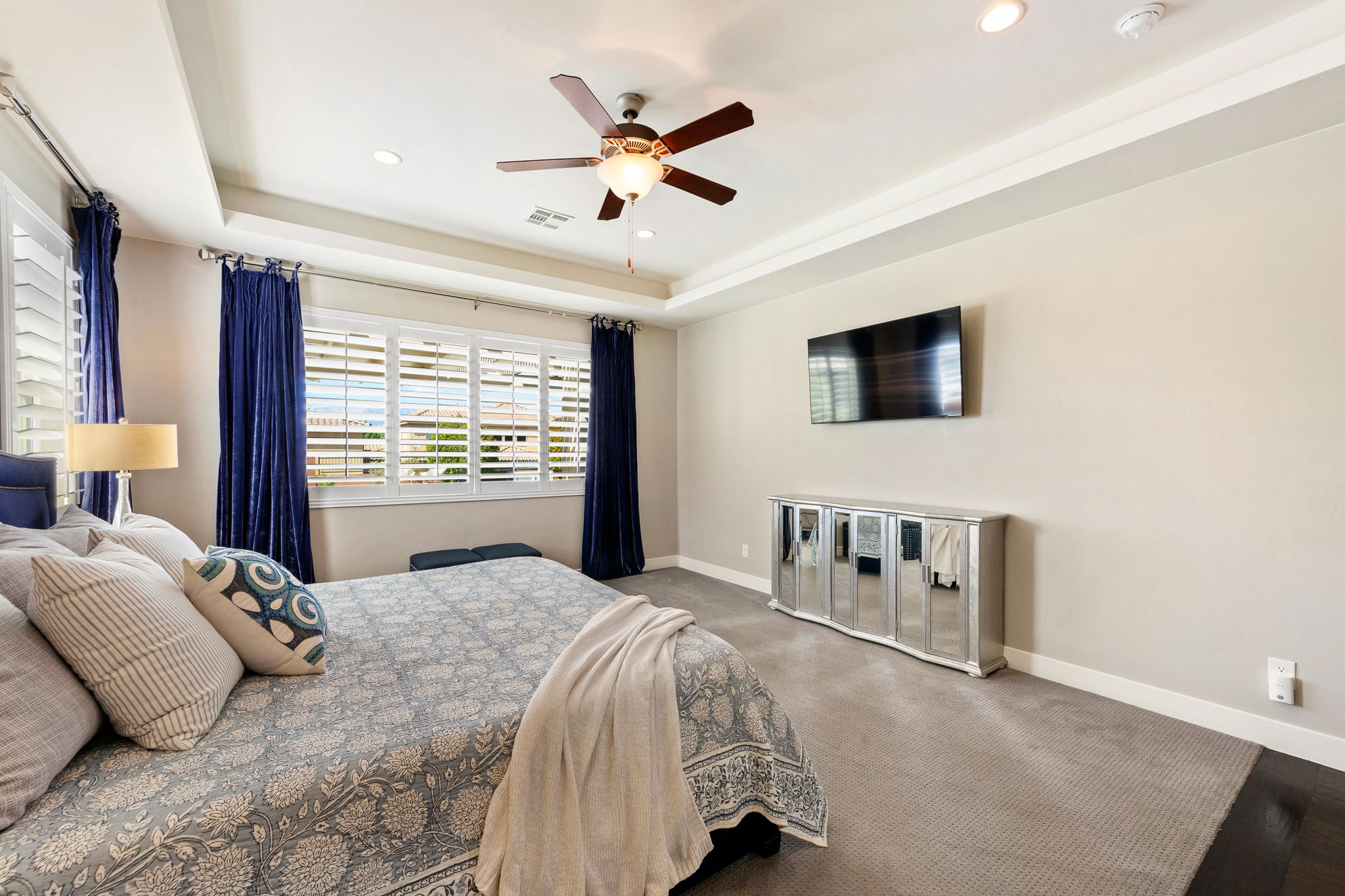Spacious bedroom featuring neutral wall tones, plush carpeting, and a tray ceiling with recessed lighting