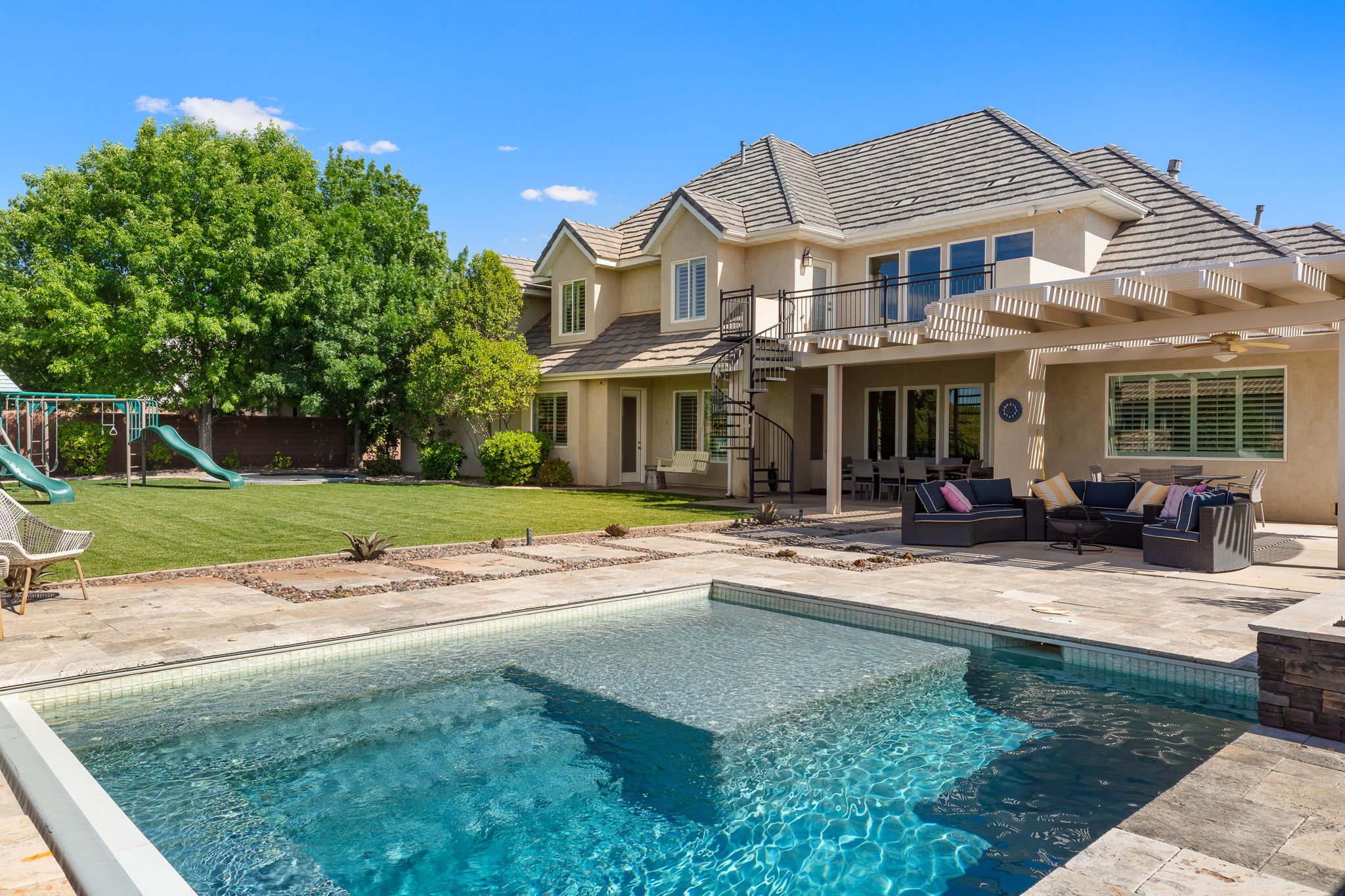 Backyard oasis featuring an in-ground swimming pool with an integrated spa, expansive paver patio, covered outdoor living area with a pergola, spiral staircase access to the upper level, and a large manicured lawn
