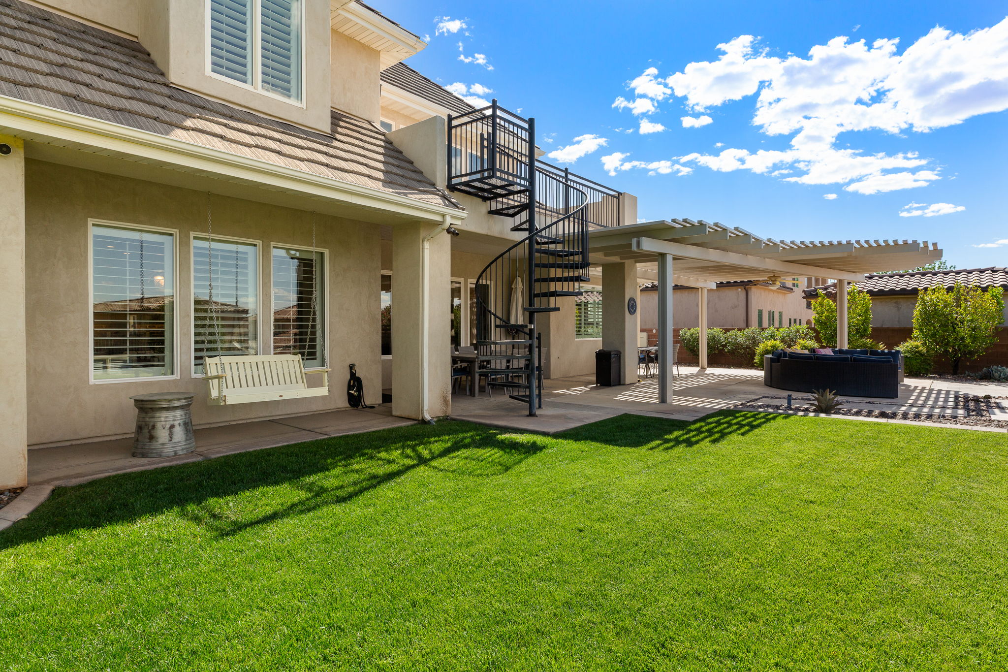 Expansive backyard featuring a lush lawn, a spiral staircase, a covered patio with a slatted roof, and a built-in outdoor seating area
