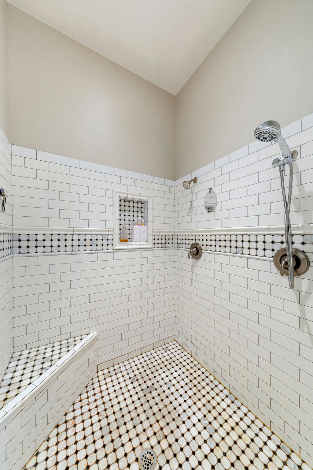 Walk-in shower featuring white subway tile, a decorative black and white mosaic accent band, and an integrated shower bench