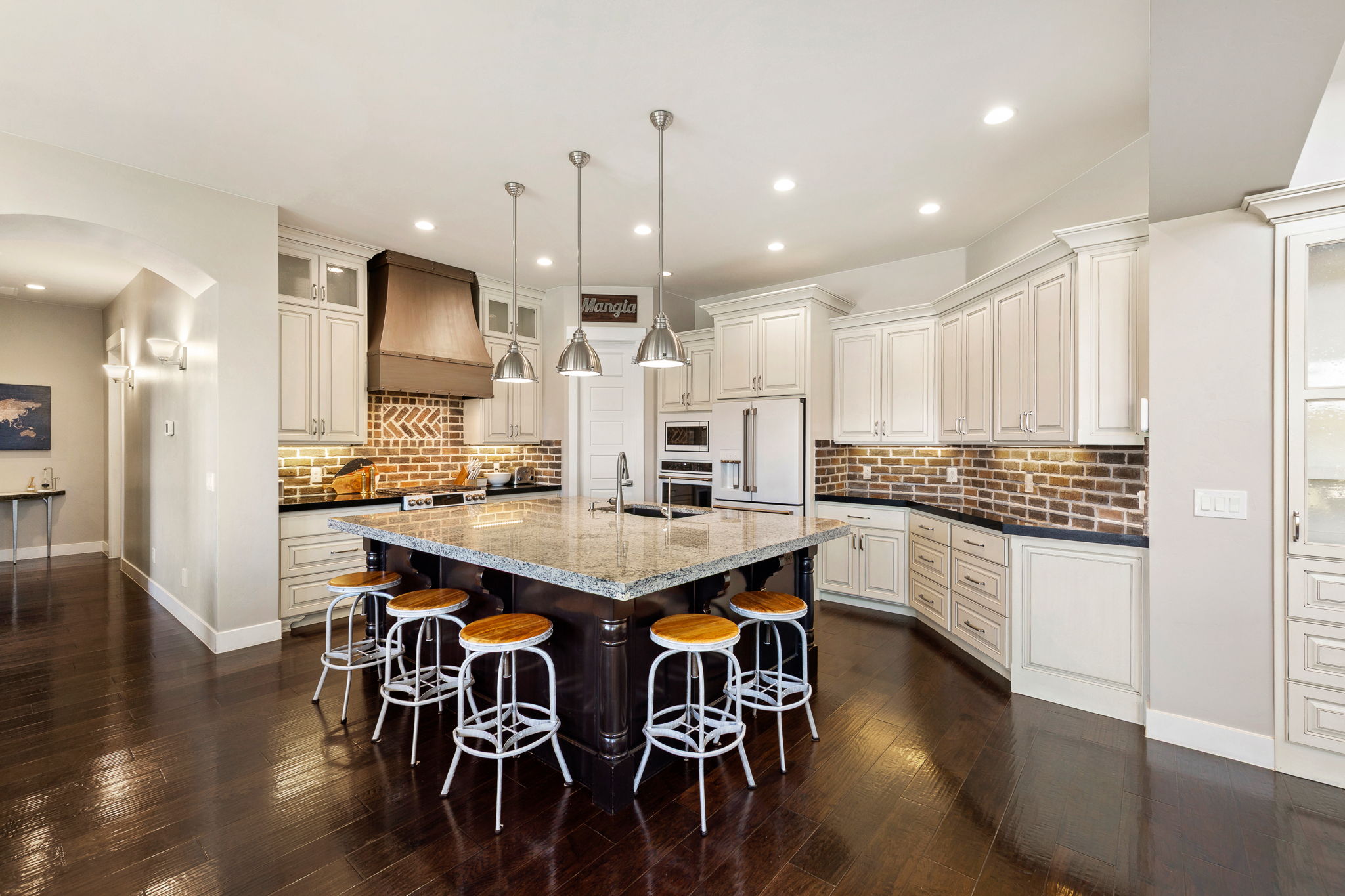 Spacious kitchen featuring a large central island with seating, a brick-patterned backsplash, white cabinetry, dark countertops, and stainless steel appliances
