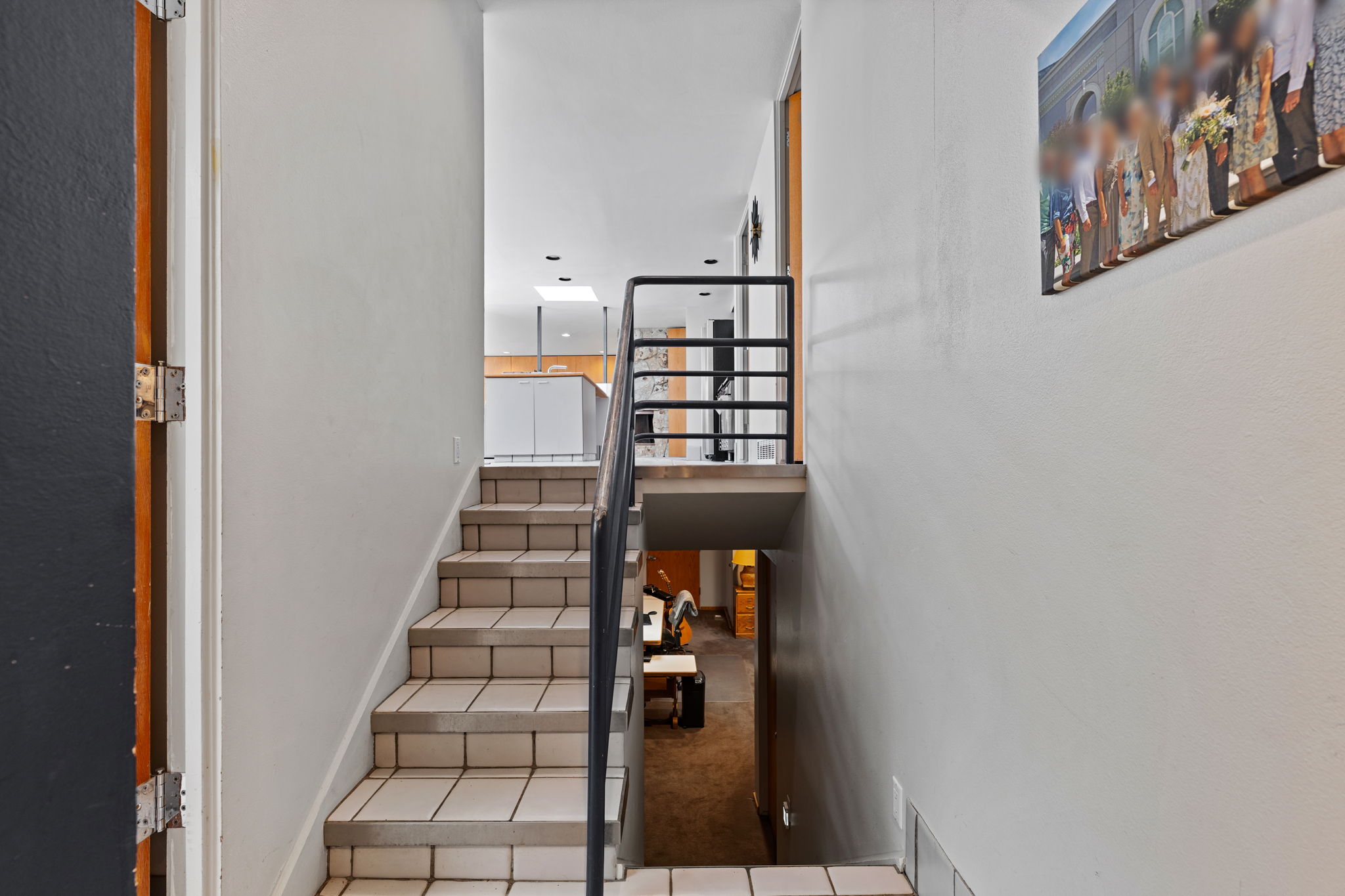 Multi-level interior featuring tile stairs with dark grout, a metal handrail, white walls, and a visible skylight