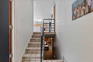 Multi-level interior featuring tile stairs with dark grout, a metal handrail, white walls, and a visible skylight