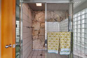 Shower enclosure featuring natural stone wall accents and white square tiling