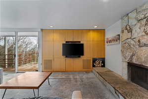 Living area featuring a floor-to-ceiling stone fireplace, built-in blonde wood cabinetry, recessed lighting, and sliding glass doors opening to an exterior deck
