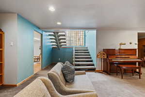 Carpeted living area featuring recessed lighting, a sliding door opening to wood-finish flooring, a staircase with glass block accents, and light blue wall details