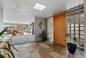 Foyer featuring flagstone flooring, a skylight, a wood-finish entry door, and glass block wall elements