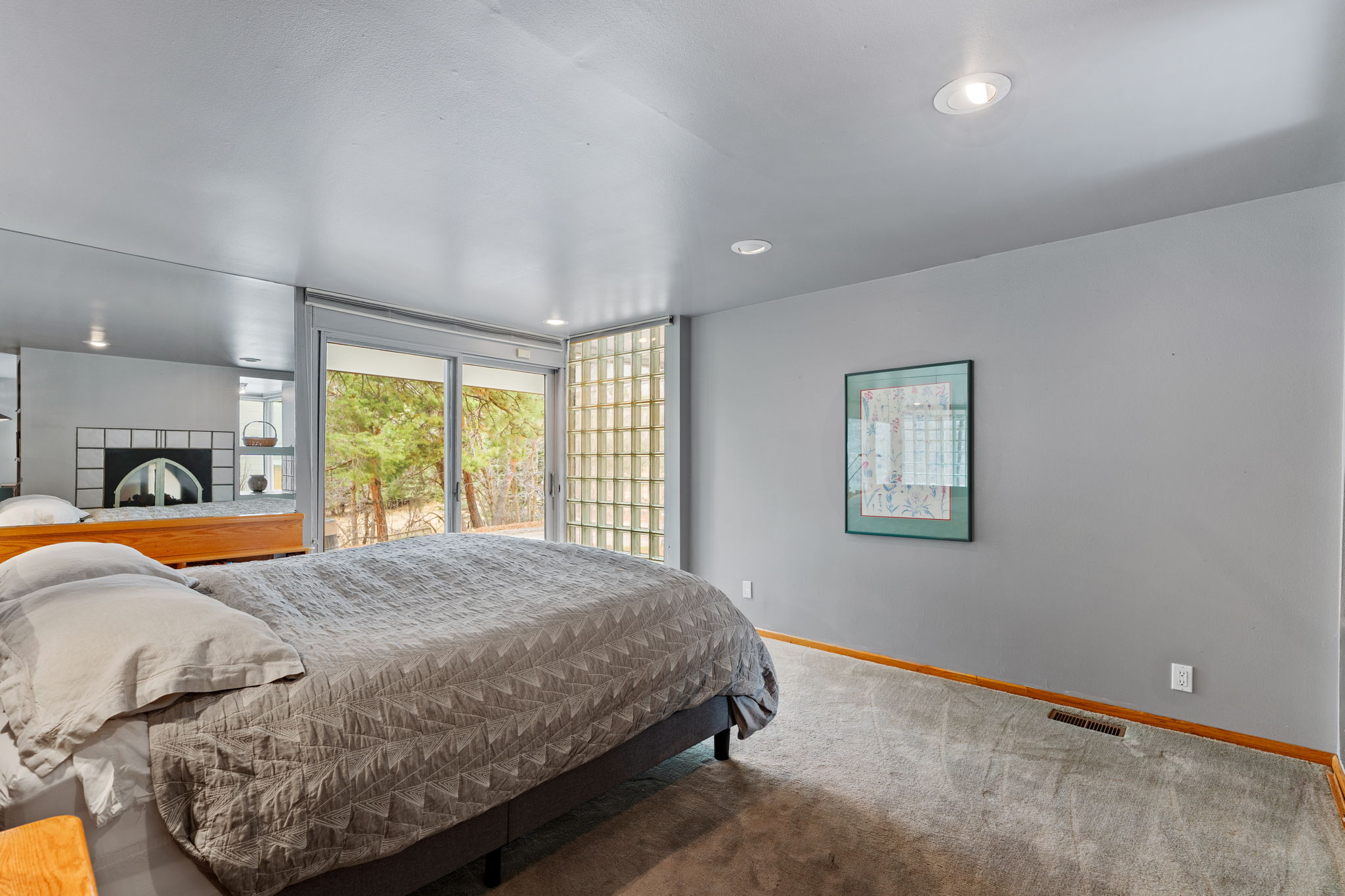Sliding glass doors opening to the exterior, recessed ceiling lighting, gray walls, light gray carpeting, and a built-in tiled fireplace with an arched opening