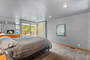 Sliding glass doors opening to the exterior, recessed ceiling lighting, gray walls, light gray carpeting, and a built-in tiled fireplace with an arched opening