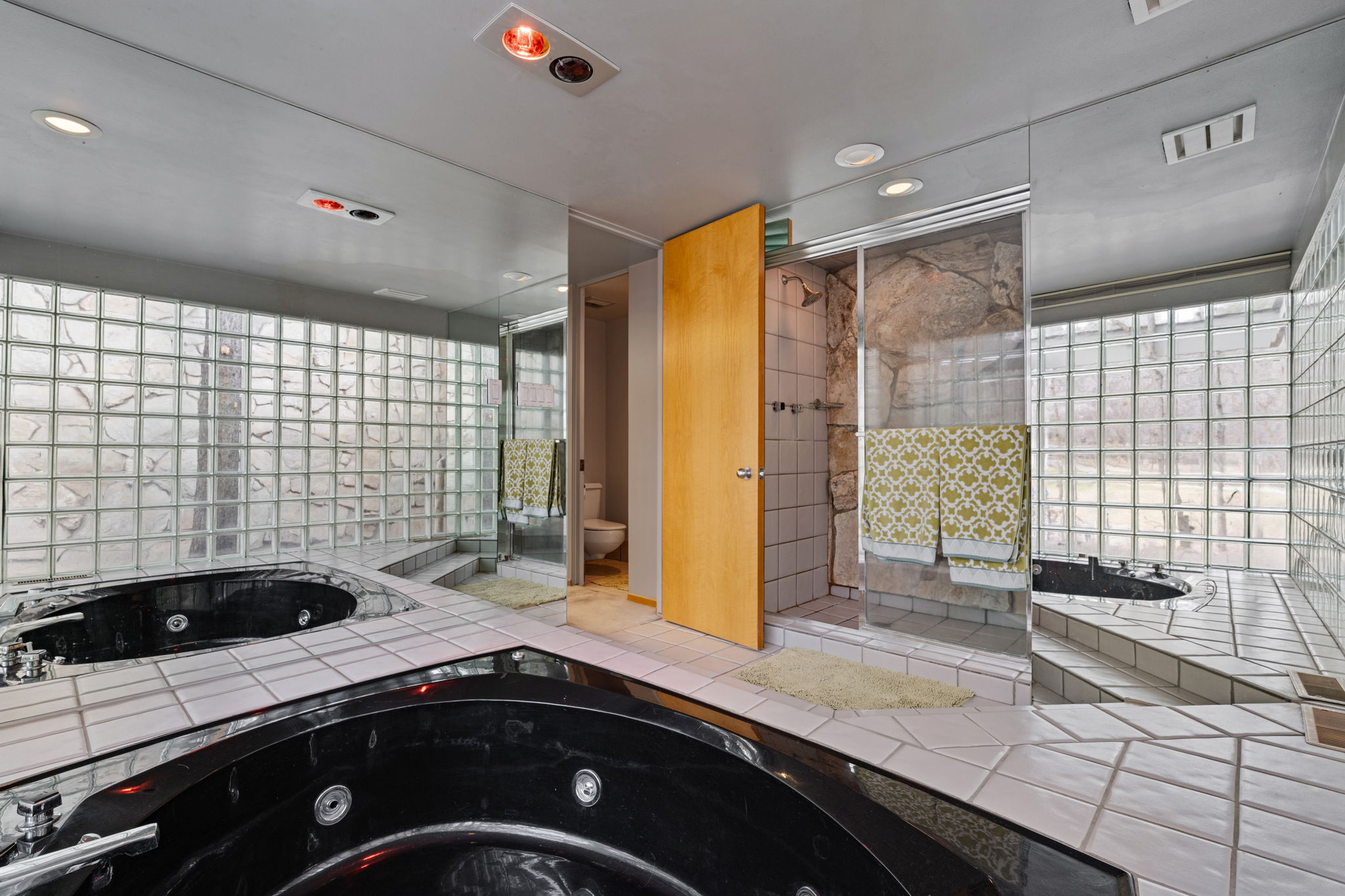 Bathroom featuring a black corner soaking tub with jetted features, a glass block wall, and white tile flooring