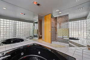 Bathroom featuring a black corner soaking tub with jetted features, a glass block wall, and white tile flooring