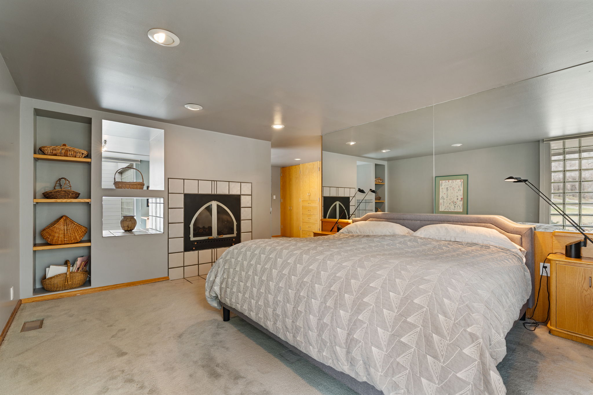 Carpeted room featuring a tiled fireplace with an arched firebox, built-in shelving, mirrored wall, and recessed lighting