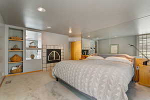 Carpeted room featuring a tiled fireplace with an arched firebox, built-in shelving, mirrored wall, and recessed lighting