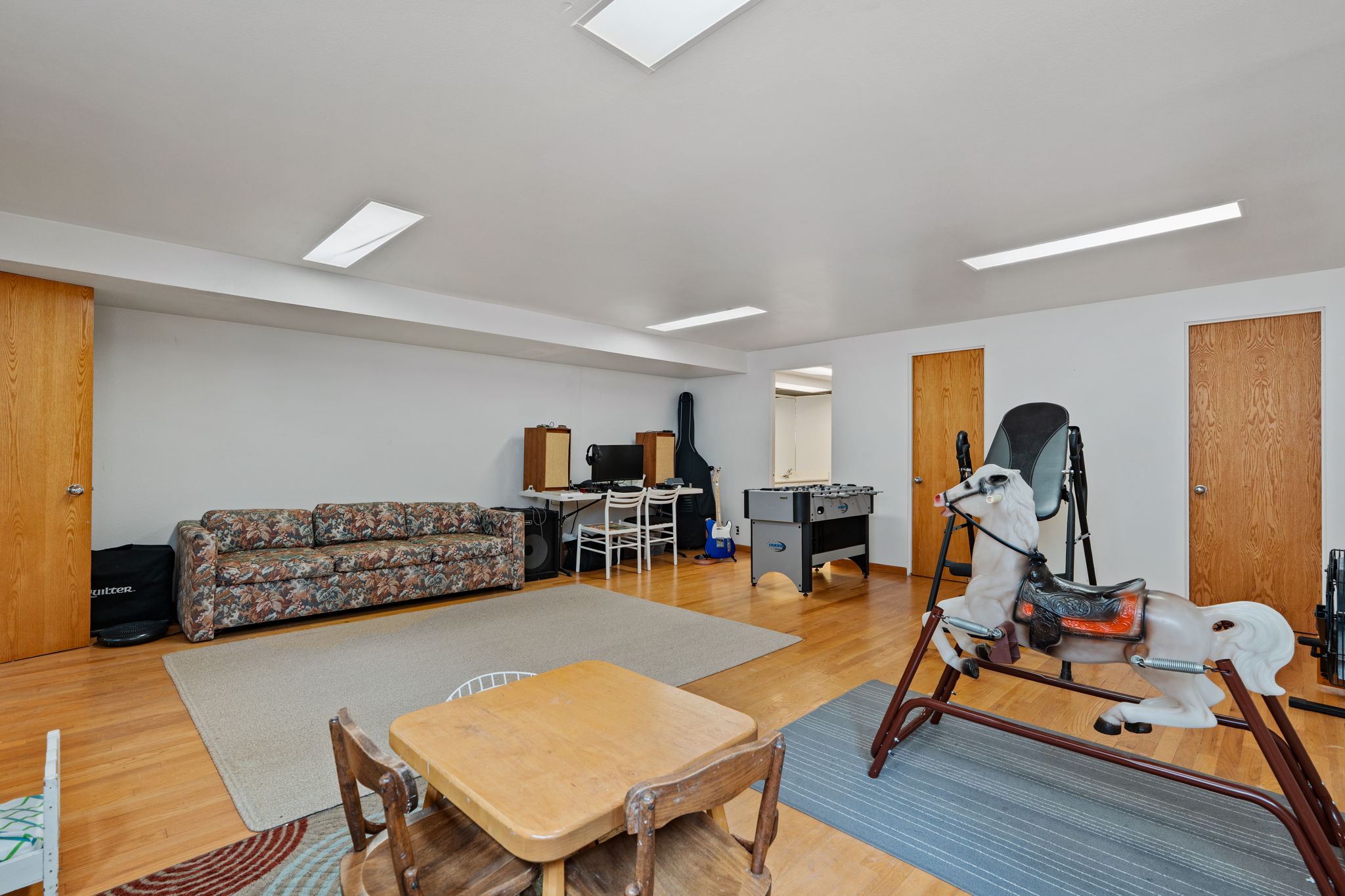 Spacious room featuring wood-finish flooring, white walls, and multiple flush-mount ceiling light fixtures